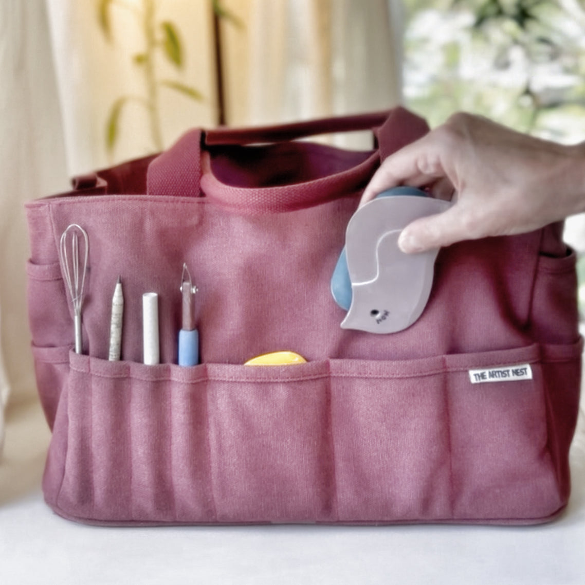Close-up of a hand placing a pottery rib into the external pocket of the red Waratah pottery tool bag. Australia
