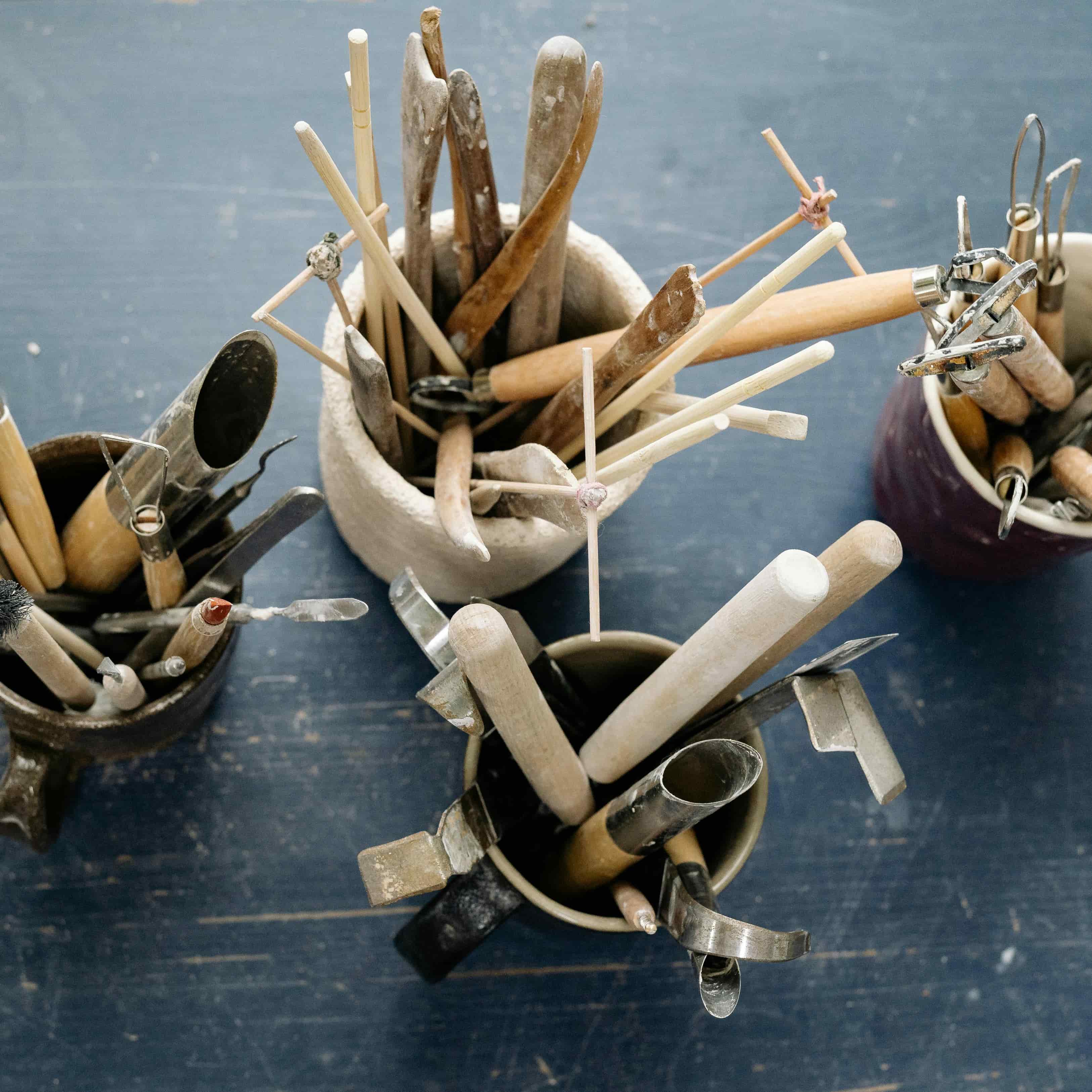 Pottery tools stored in jars and containers in a cluttered studio setup, showing the challenge of keeping tools organised.