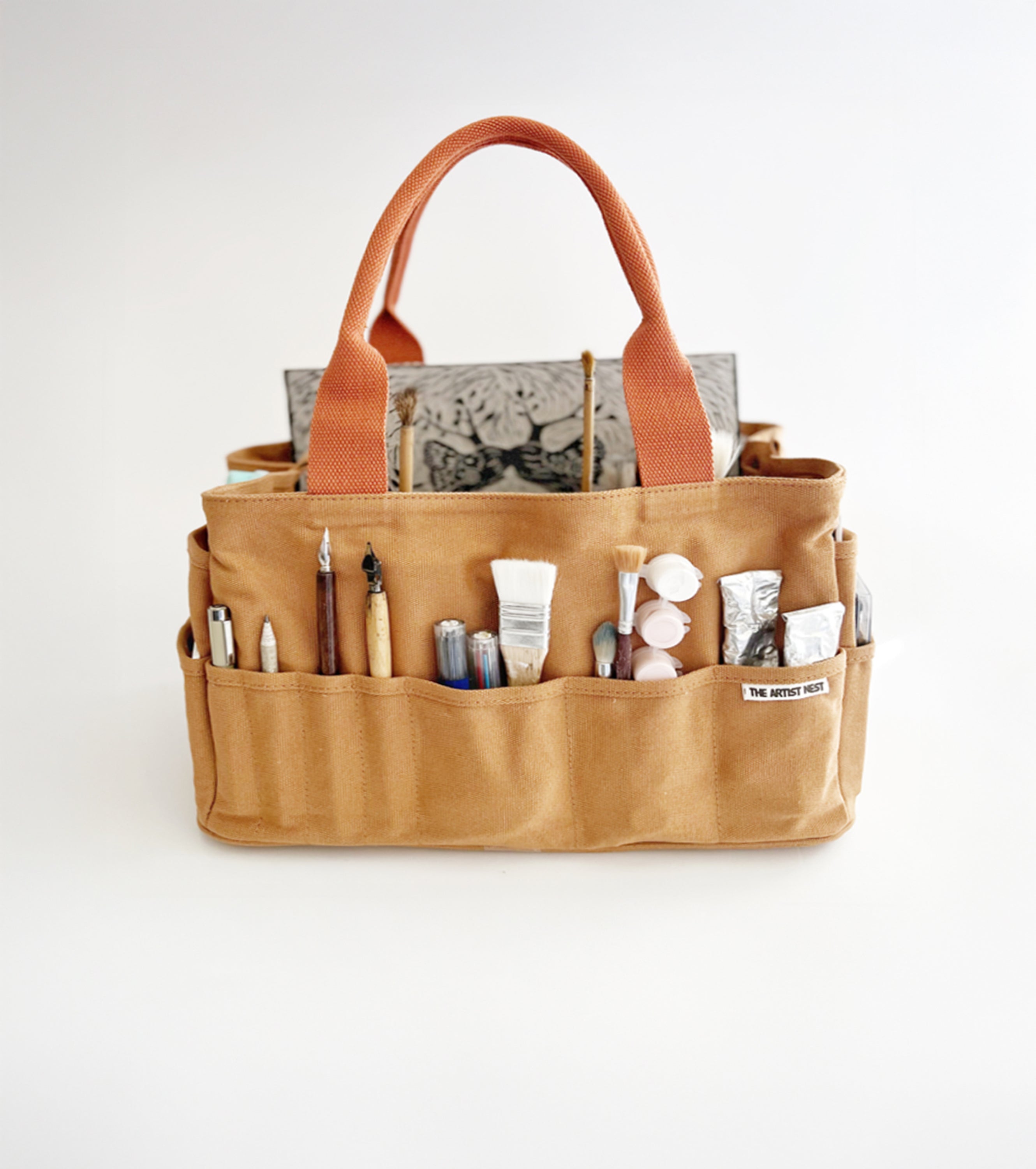 Outback artist bag with 27 pockets filled with drawing and painting tools, brushes, pens, paint, and a linocut artwork, designed in Byron Bay.