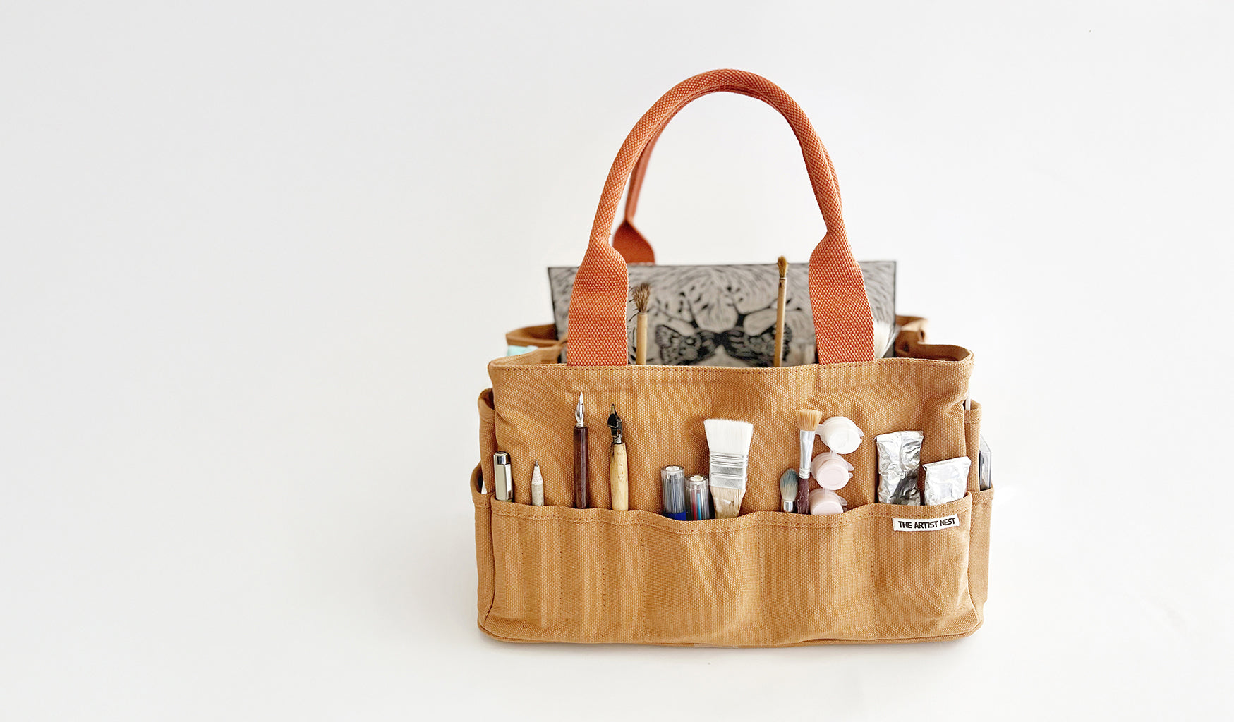 Outback artist bag with multi 27 pockets filled with drawing and painting tools, brushes, pens, paint, and a linocut artwork, designed in Byron Bay by Mon Manabu