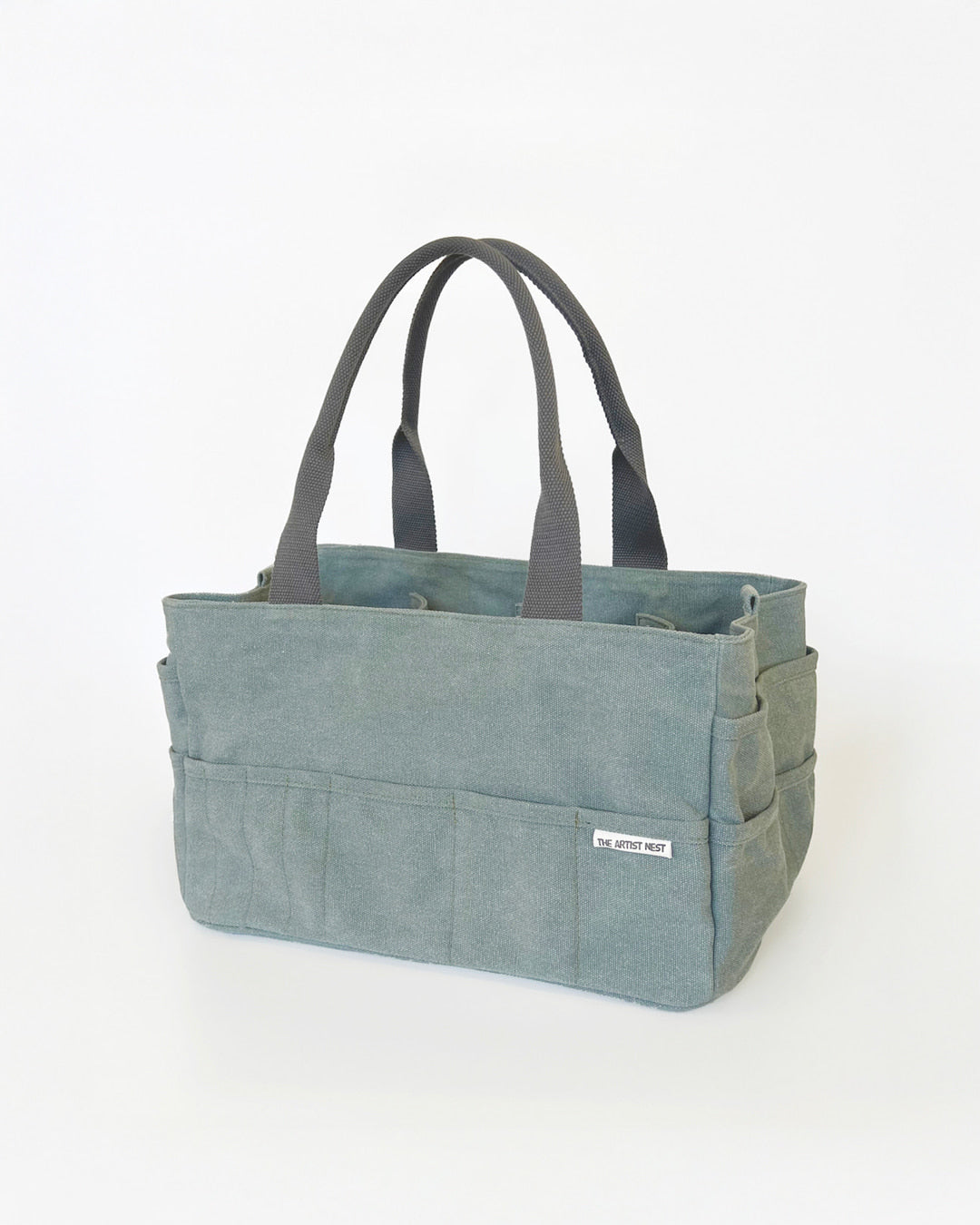 Eucalypt green Artist Bag shown in a diagonal angle, canvas artist supply bag with 18 exterior pockets and nine tall interior pockets designed for creators in Australia.