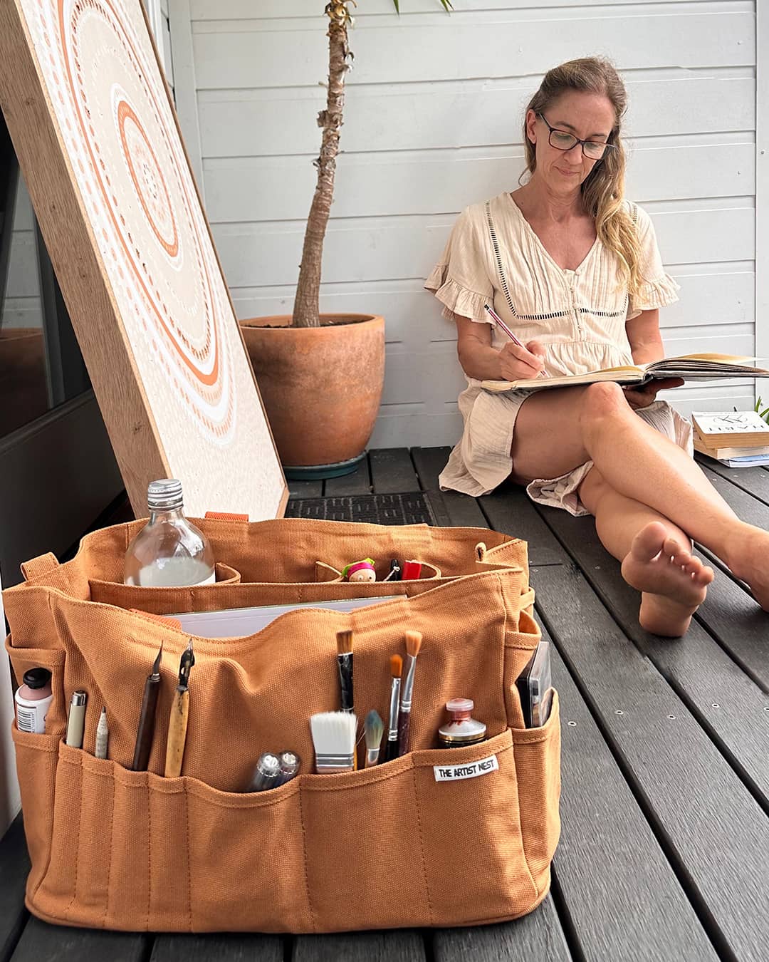 Outback Artist Bag filled with pencils, markers and drawing tools beside an artist sketching in Australia, ideal for illustrators and painters needing organised pockets.