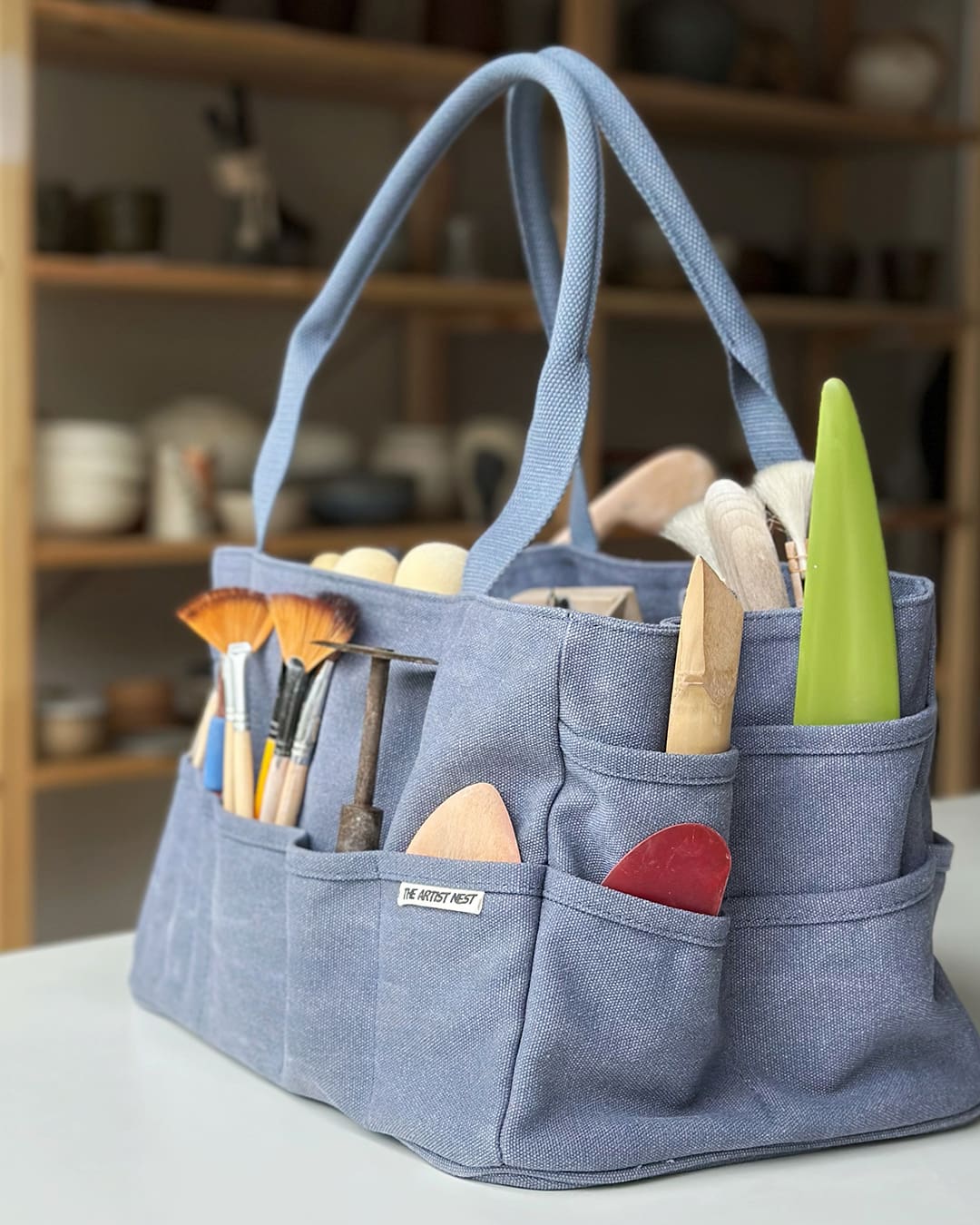 The Pass blue pottery tool bag filled with ceramic tools, sponges, ribs and brushes organised across exterior and interior pockets.