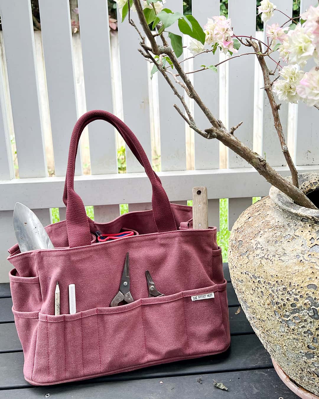 Waratah red Artist Bag filled with gardening tools beside a vibrant bougainvillea, multipurpose canvas tool bag for makers and gardeners in Australia.