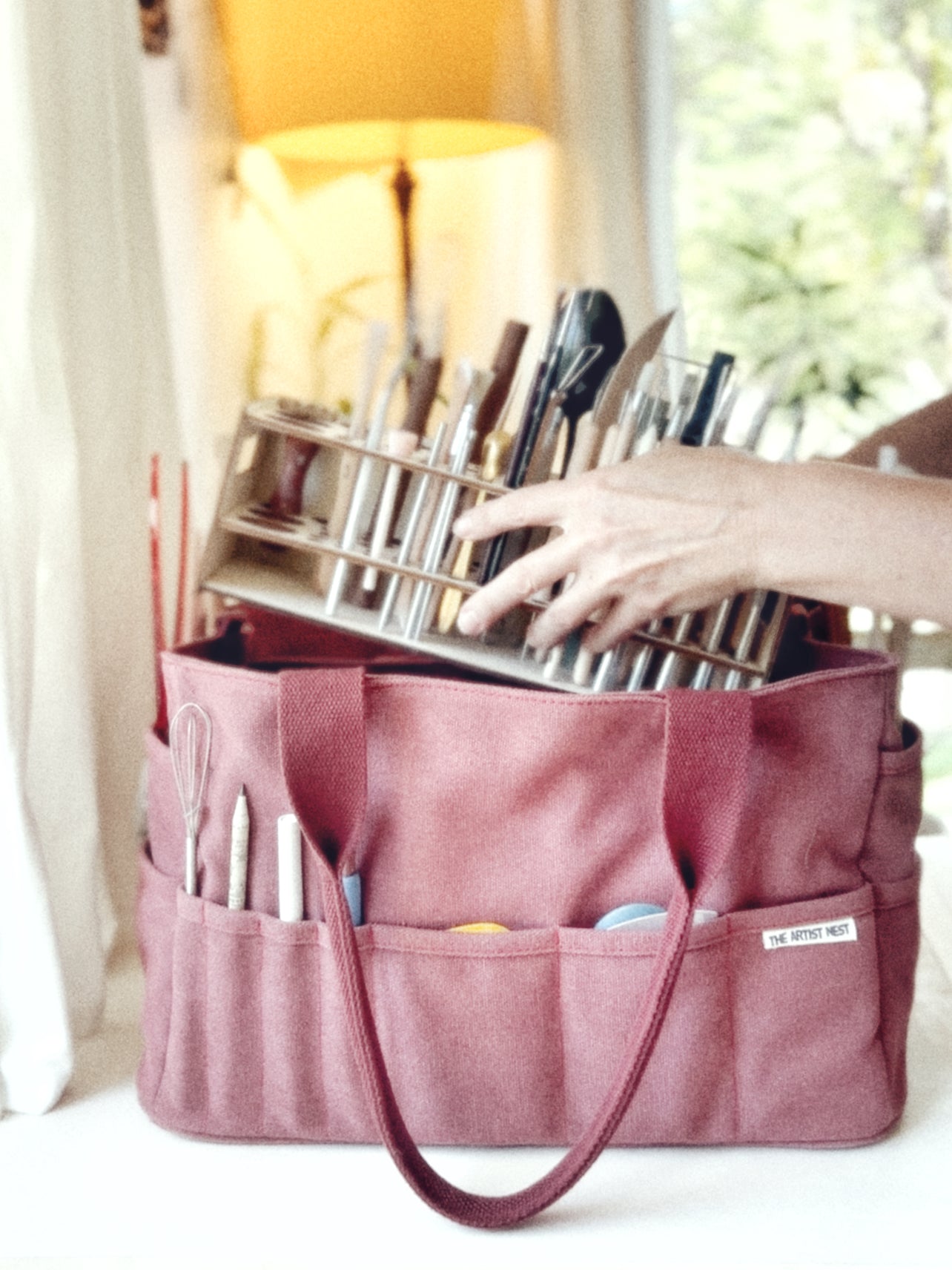 Red Waratah pottery tool bag with a wooden tool rack fully loaded with pottery tools being placed inside the bag.